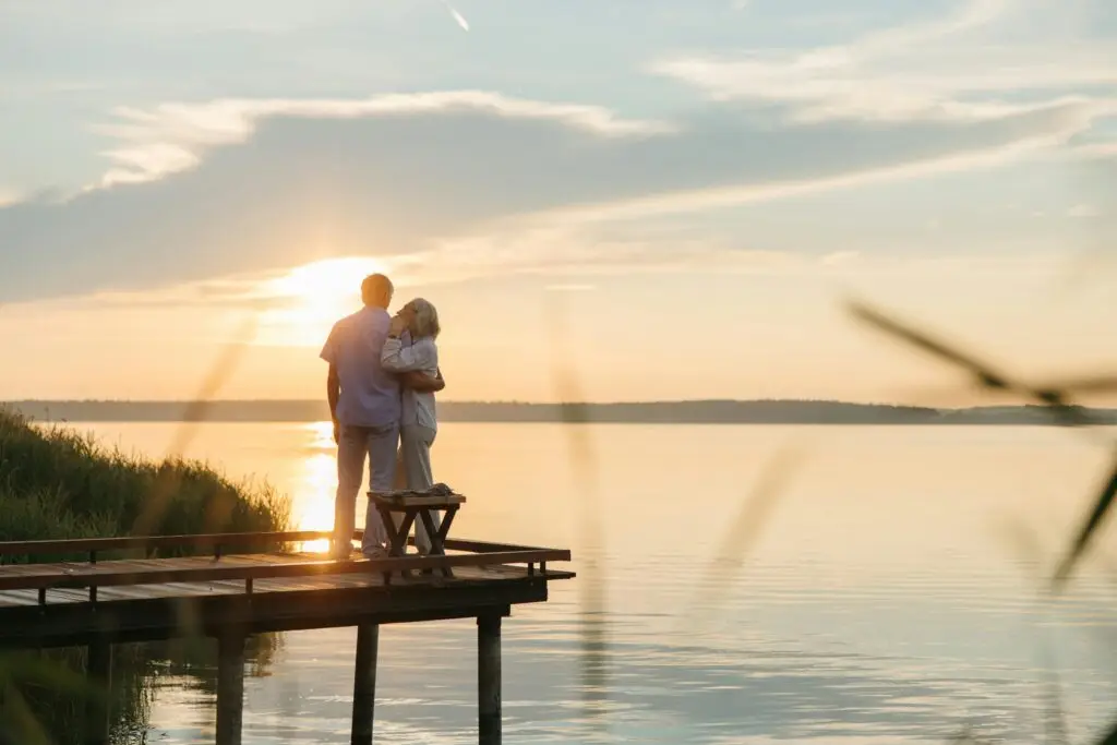 A senior couple embraces on a wooden dock at sunset, exuding tranquility and affection.